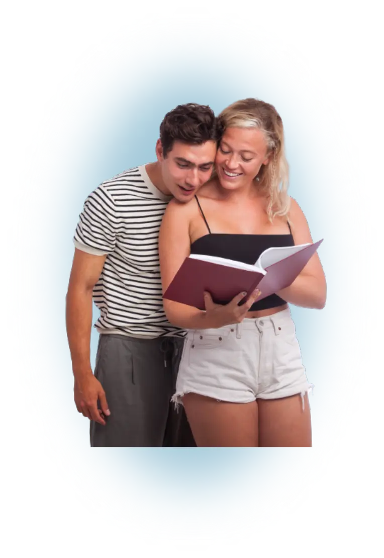 A young woman is holding a book and a young man is standing behind her looking at the book.